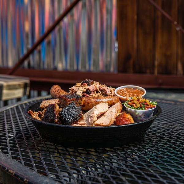 A large platter of barbecue meats, including brisket, pulled pork, sausage, and chicken, with sides of baked beans and coleslaw.