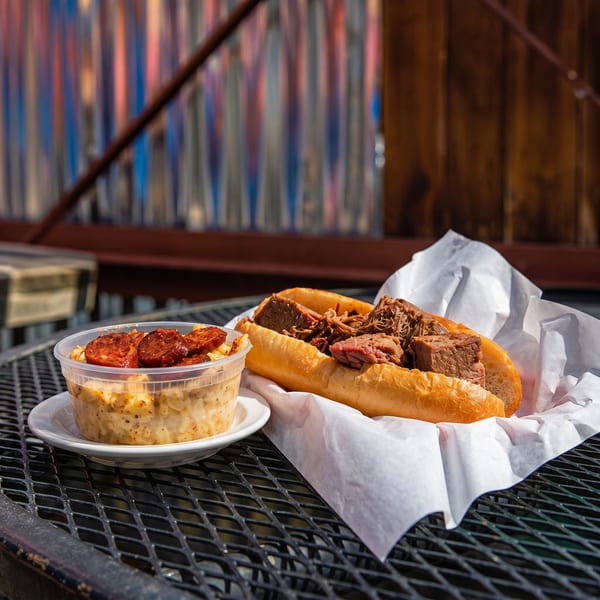 A brisket sandwich and a side of mac and cheese with chorizo on a metal table.