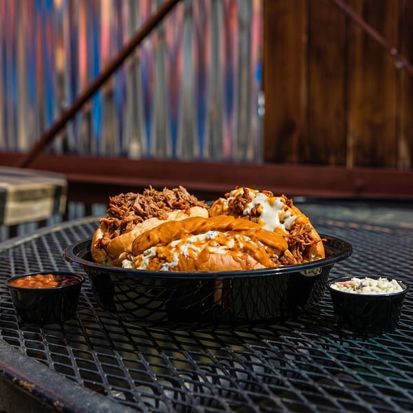 Three loaded hot dogs with various toppings, baked beans, and coleslaw on a black mesh table.