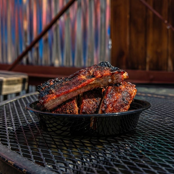 Close-up of barbecue ribs in a black basket on a metal grate table.
