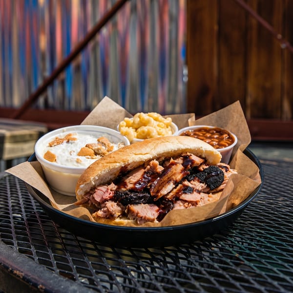 A pulled pork sandwich with sides of baked beans, mac and cheese, and banana pudding.